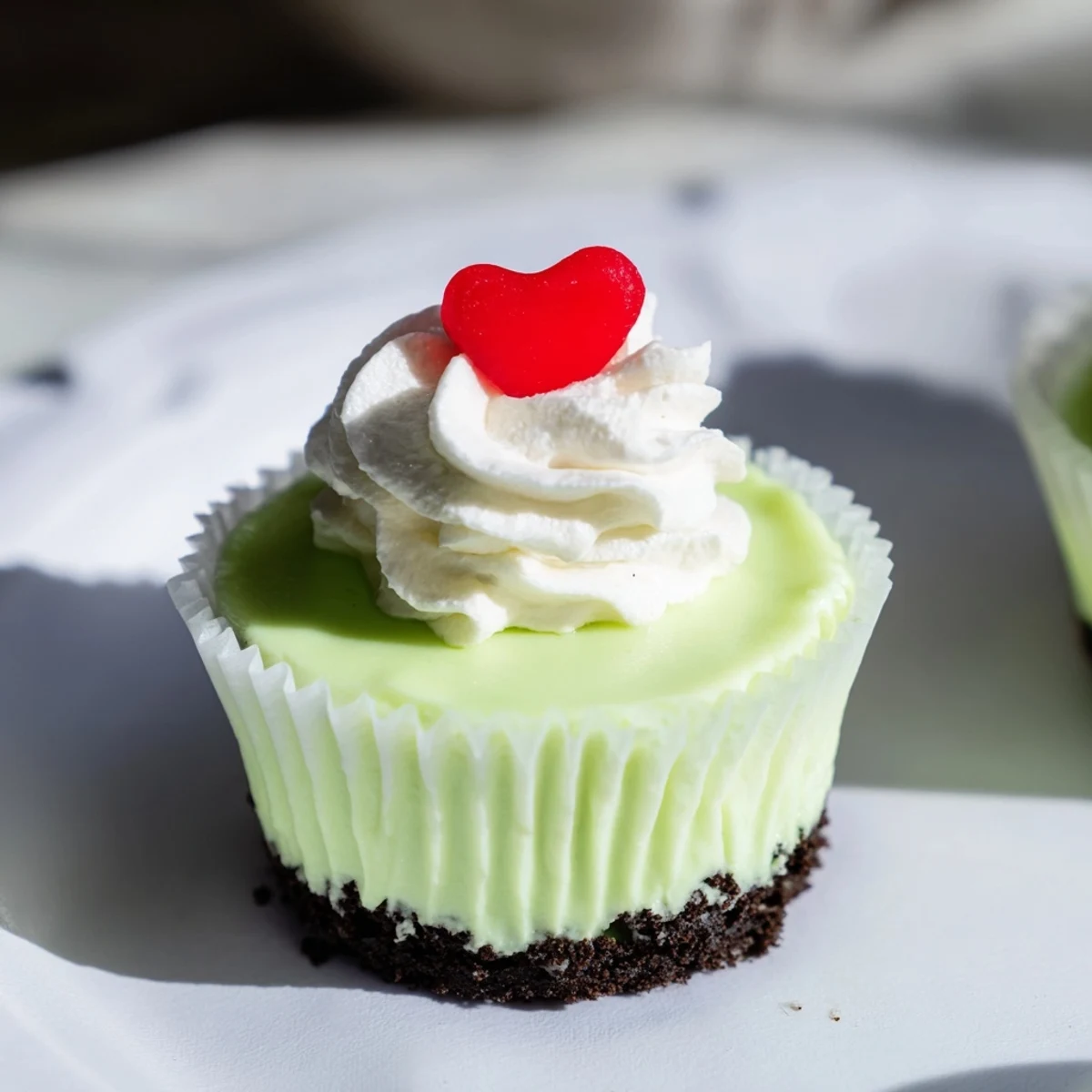 Festive Grinch Mini Cheesecakes topped with whipped cream and red heart sprinkles, a perfect holiday dessert.