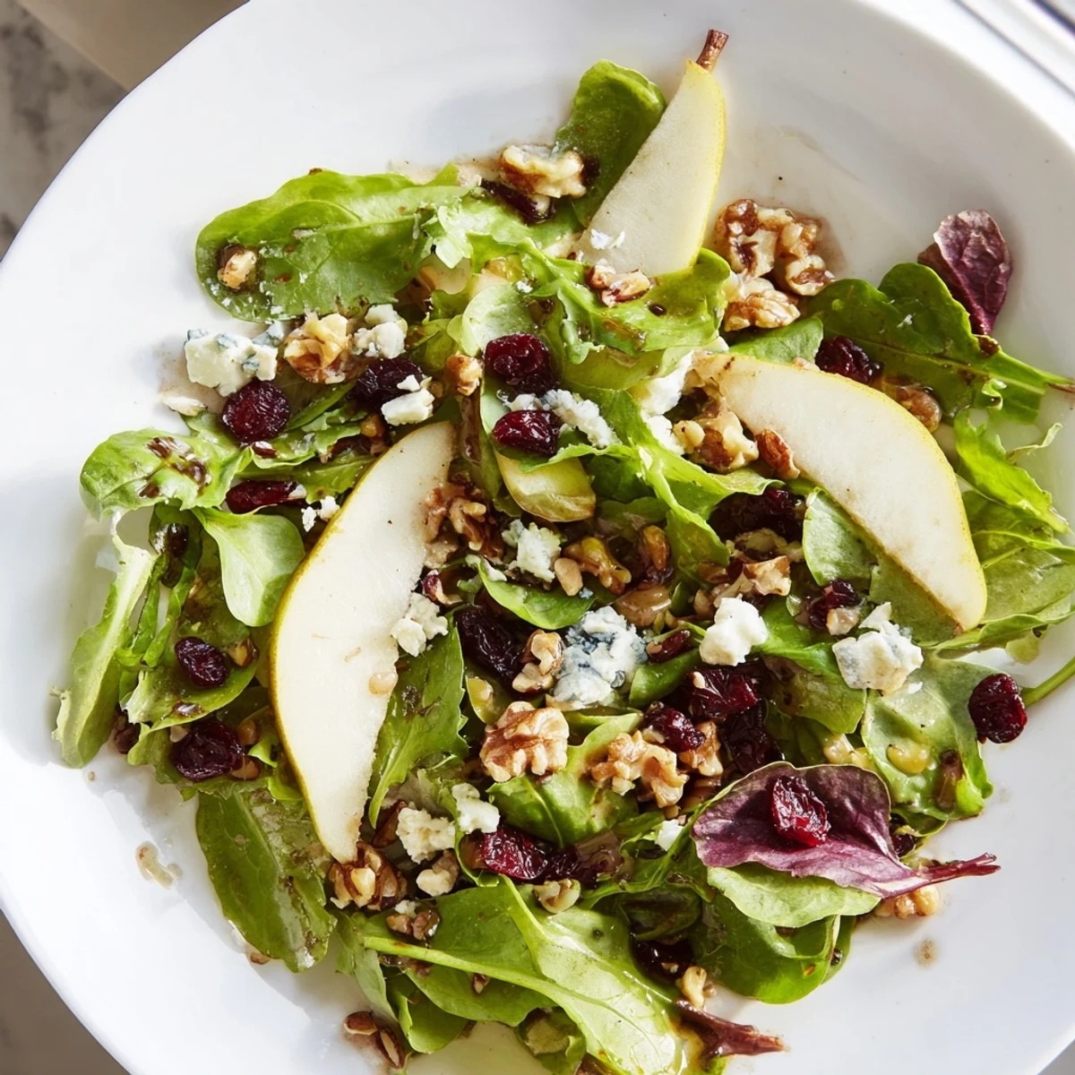 A vibrant mixed green salad with sweet pears, tangy Gorgonzola, crunchy walnuts, and a honey-balsamic dressing, ready to serve.