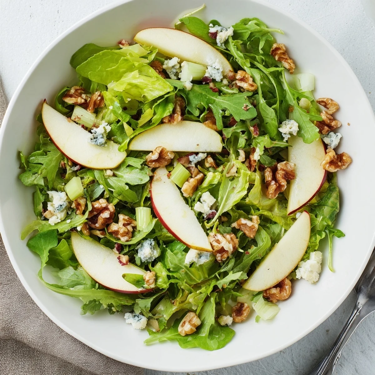 Freshly sliced apples and walnuts arranged on salad greens with a light, zesty vinaigrette, perfect for a healthy side.