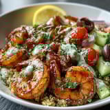 A colorful Mediterranean Shrimp Bowl features diced cucumbers, cherry tomatoes, and Kalamata olives, garnished with fresh parsley and lemon wedges.