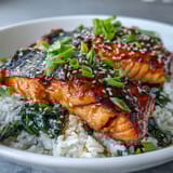 Freshly cooked miso glazed salmon bowl served with bright greens, fluffy rice, and a side of lime wedges for zest.