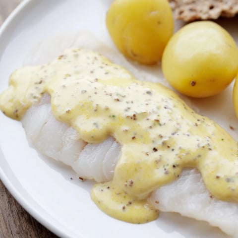 Flaky Norwegian lutefisk, bathed in creamy mustard sauce, ready for serving with potatoes and crispbread.