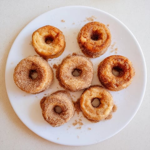 Freshly air-fried Air Fryer Cinnamon Sugar Donuts, golden brown and glistening with sweet spice, served warm beside a steaming mug of coffee.