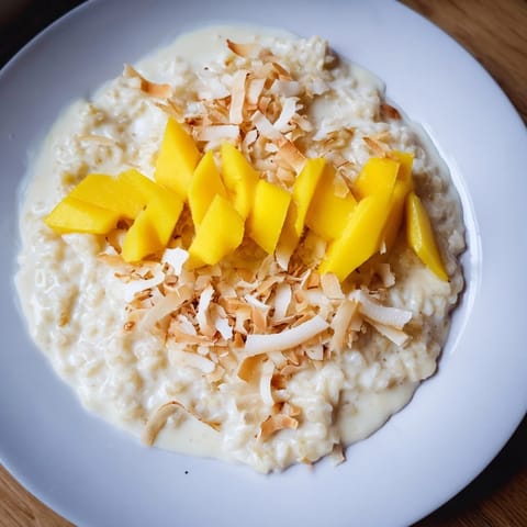 Warm, creamy toasted Coconut Rice Pudding, topped with golden coconut flakes and ripe mango slices.