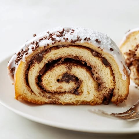 Overhead view of Nutella Chocolate Chip Rolls arranged in a pan, glistening with a sweet powdered sugar glaze and a sprinkle of extra chocolate chips.
