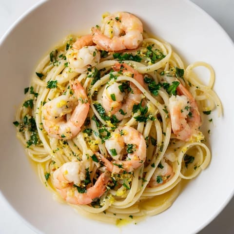 A skillet of Garlic Butter Shrimp Linguine with plump, pink shrimp served alongside al dente pasta and lemon wedges.