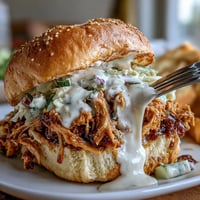 Juicy smoked pulled chicken sandwiches piled high, dripping with creamy white BBQ sauce.