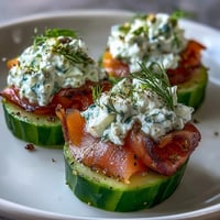 Smoked salmon cucumber bites with creamy herb cheese on crisp cucumber rounds, perfect for elegant appetizers.  
